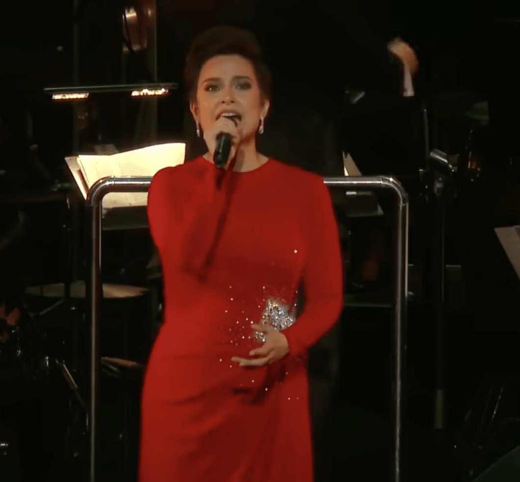 Lea Solanga sings on-stage in a red dress.